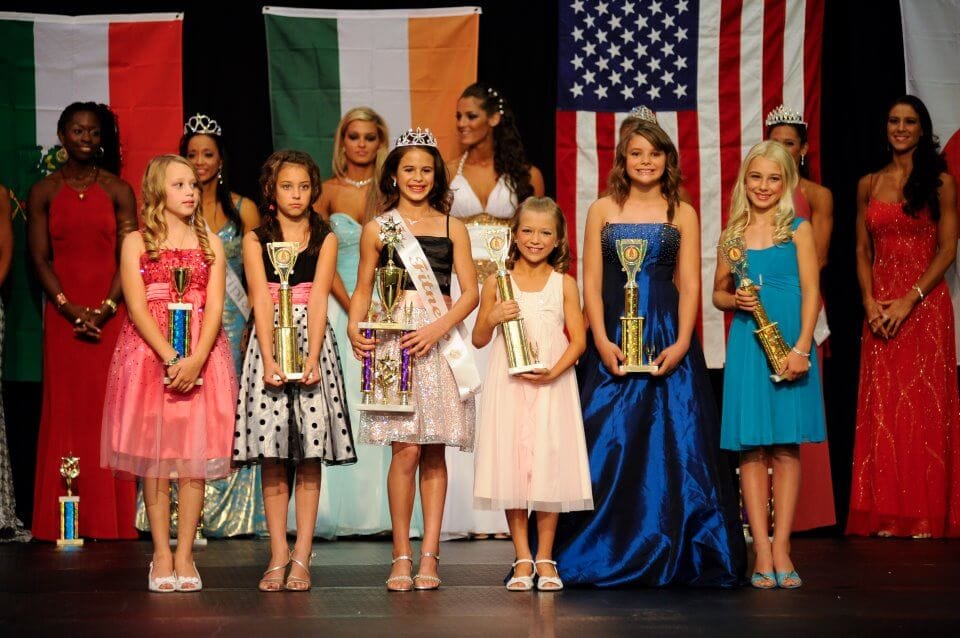 Stage is filled with junior competitors holding their trophies and smiling