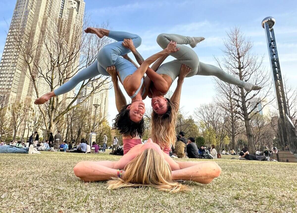 Three AcroYogi performing in the park. Two women are held aloft by a man with his feet while laying in the grass